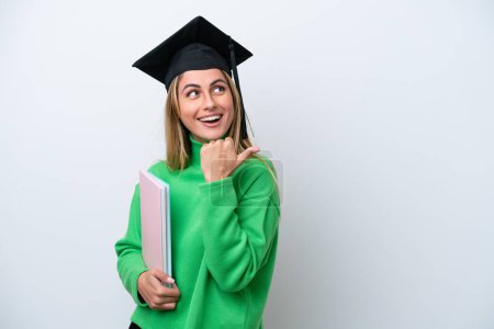 Téléchargez les photos : Jeune diplômée de l'université isolée sur fond blanc pointant vers le côté pour présenter un produit - en image libre de droit