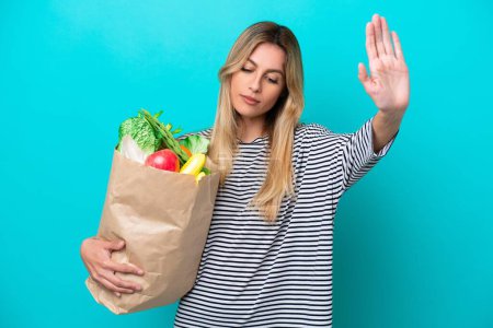 Photo for Young Uruguayan woman holding a grocery shopping bag isolated on blue background making stop gesture and disappointed - Royalty Free Image