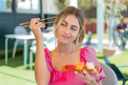 Photo for Young blonde woman holding sashimi at outdoors - Royalty Free Image