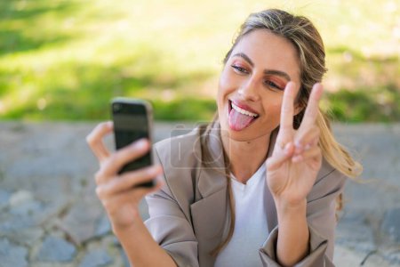Téléchargez les photos : Jeune jolie femme uruguayenne blonde à l'extérieur en utilisant un téléphone mobile - en image libre de droit