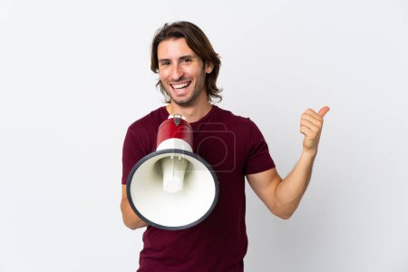 Téléchargez les photos : Jeune homme beau isolé sur fond blanc criant à travers un mégaphone et le côté pointant - en image libre de droit