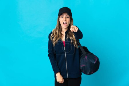 Photo for Young Romanian sport woman with sport bag isolated on blue background surprised and pointing front - Royalty Free Image