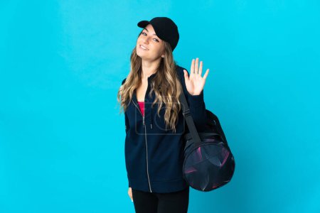 Photo for Young Romanian sport woman with sport bag isolated on blue background saluting with hand with happy expression - Royalty Free Image
