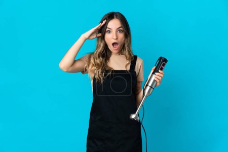 Photo for Romanian woman using hand blender isolated on blue background with surprise expression - Royalty Free Image