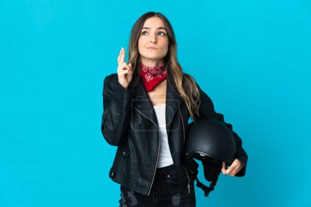 Photo for Romanian woman holding a motorcycle helmet isolated on blue background with fingers crossing and wishing the best - Royalty Free Image