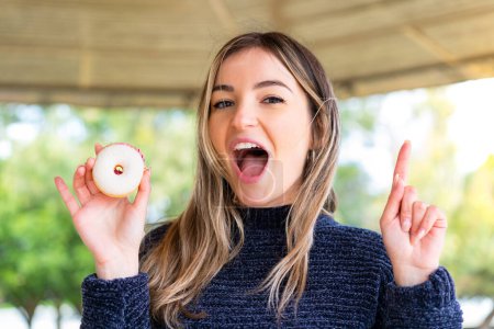 Photo for Young pretty Romanian woman holding a donut at outdoors pointing up a great idea - Royalty Free Image