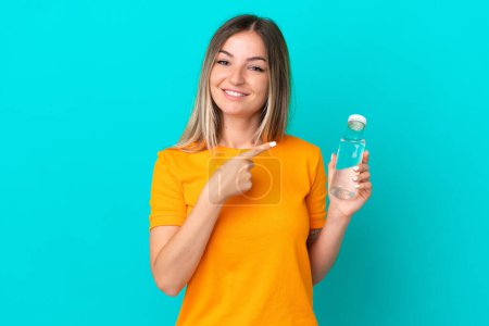 Photo for Young Romanian woman with a bottle of water isolated on blue background pointing to the side to present a product - Royalty Free Image