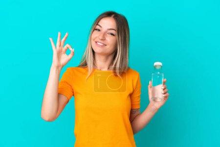 Photo for Young Romanian woman with a bottle of water isolated on blue background showing ok sign with fingers - Royalty Free Image