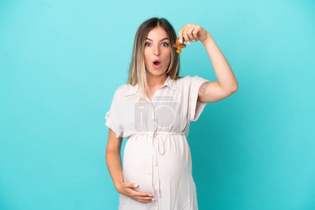 Photo for Young Romanian woman isolated on blue background pregnant and holding a pacifier with surprised expression - Royalty Free Image