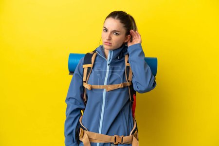 Téléchargez les photos : Jeune alpiniste femme avec un grand sac à dos sur fond jaune isolé ayant des doutes - en image libre de droit