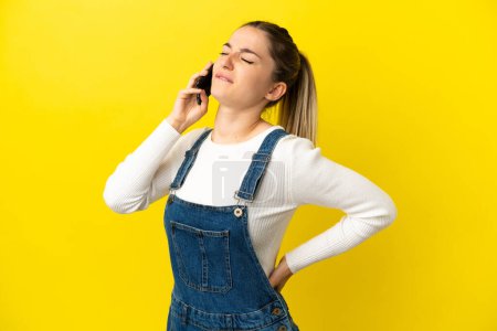 Photo for Young woman using mobile phone over isolated yellow background suffering from backache for having made an effort - Royalty Free Image