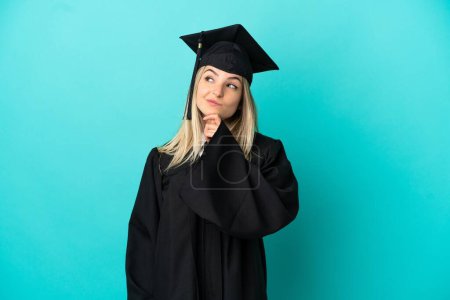 Foto de Joven graduado universitario sobre fondo azul aislado y mirando hacia arriba - Imagen libre de derechos