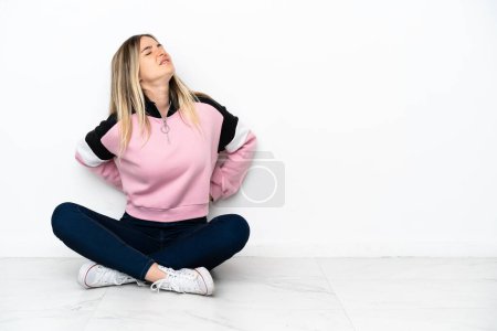 Photo for Young woman sitting on the floor at indoors suffering from backache for having made an effort - Royalty Free Image