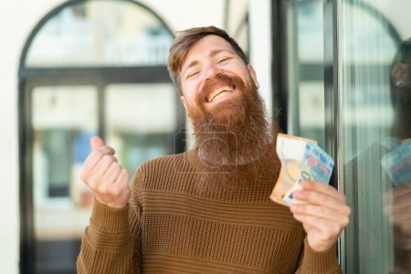 Téléchargez les photos : Rousse homme avec barbe prendre beaucoup d'argent avec expression heureuse - en image libre de droit