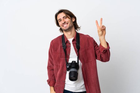 Téléchargez les photos : Jeune photographe homme isolé sur fond blanc souriant et montrant signe de victoire - en image libre de droit