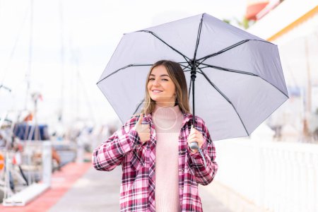 Téléchargez les photos : Jeune jolie roumaine tenant un parapluie à l'extérieur avec les pouces levés parce que quelque chose de bon est arrivé - en image libre de droit