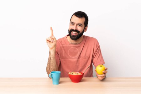 Foto de Hombre caucásico desayunando en una mesa mostrando y levantando un dedo en señal de la mejor. - Imagen libre de derechos