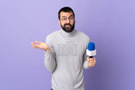 Téléchargez les photos : Reporter adulte homme avec barbe tenant un microphone sur fond violet isolé ayant des doutes - en image libre de droit