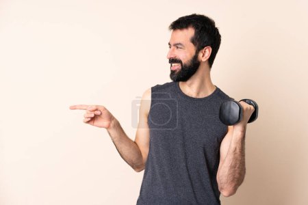 Photo for Caucasian sport man with beard making weightlifting over isolated background pointing finger to the side - Royalty Free Image