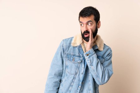 Téléchargez les photos : Homme caucasien avec barbe sur fond isolé chuchotant quelque chose avec geste de surprise tout en regardant sur le côté - en image libre de droit