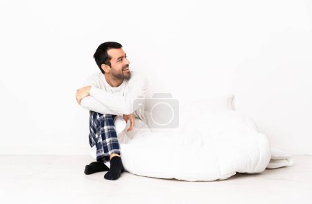 Téléchargez les photos : Homme caucasien en pyjama assis sur le sol à l'intérieur regardant vers le côté et souriant - en image libre de droit
