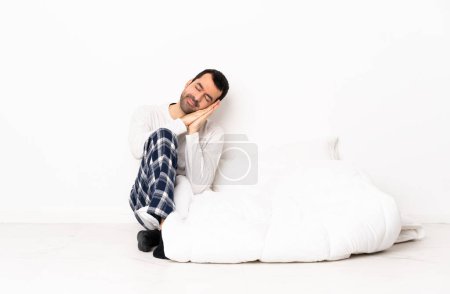 Foto de Hombre caucásico en pijama sentado en el suelo en el interior haciendo gesto de sueño en expresión dorable - Imagen libre de derechos