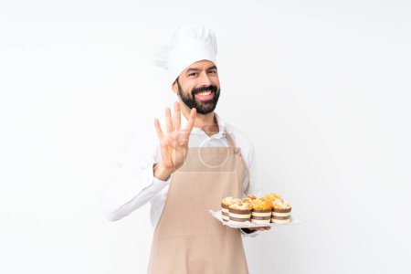 Foto de Joven sosteniendo pastel de magdalenas sobre fondo blanco aislado feliz y contando cuatro con los dedos - Imagen libre de derechos