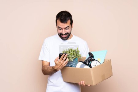 Foto de Hombre sosteniendo una caja y moviéndose en un nuevo hogar sobre un fondo aislado sorprendido y enviando un mensaje - Imagen libre de derechos