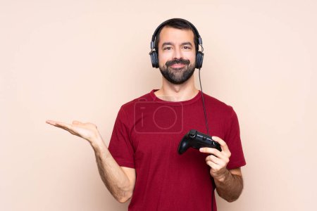 Foto de Hombre jugando con un controlador de videojuegos sobre una pared aislada sosteniendo un espacio de copia imaginario en la palma de la mano para insertar un anuncio - Imagen libre de derechos