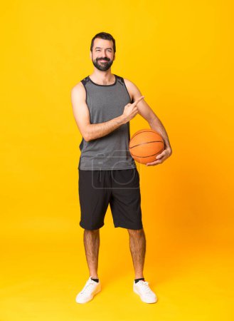 Photo for Full-length shot of man over isolated yellow background playing basketball and pointing to the lateral - Royalty Free Image