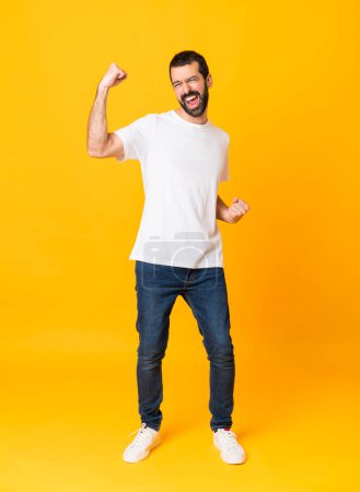 Photo for Full-length shot of man with beard over isolated yellow background celebrating a victory - Royalty Free Image