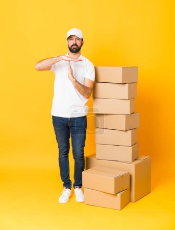 Photo for Full-length shot of delivery man among boxes over isolated yellow background making time out gesture - Royalty Free Image