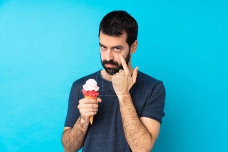 Téléchargez les photos : Jeune homme avec une crème glacée cornet sur fond bleu isolé montrant quelque chose - en image libre de droit