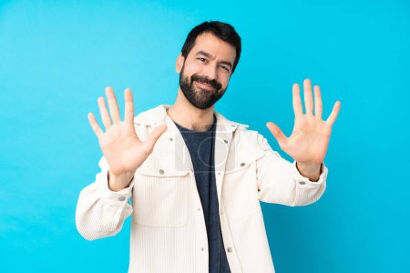 Téléchargez les photos : Jeune homme beau avec veste en velours côtelé blanc sur fond bleu isolé comptant dix avec les doigts - en image libre de droit