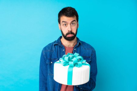 Photo for Young handsome man with a big cake over isolated blue background with sad and depressed expression - Royalty Free Image