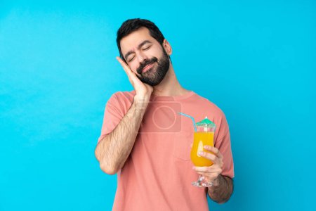 Photo for Young man over holding a cocktail over isolated blue background making sleep gesture in dorable expression - Royalty Free Image