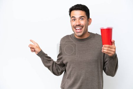 Photo for Young handsome man holding soda over isolated white background surprised and pointing finger to the side - Royalty Free Image