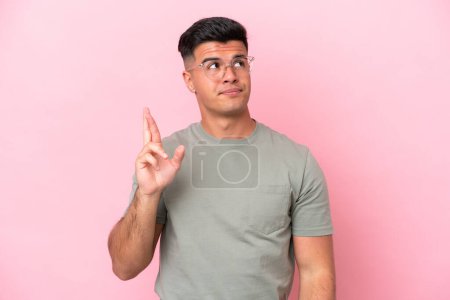 Photo for Young caucasian handsome man isolated on pink background with fingers crossing and wishing the best - Royalty Free Image