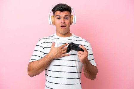 Foto de Joven hombre guapo jugando con un controlador de videojuegos aislado sobre fondo rosa sorprendido y sorprendido mientras mira a la derecha - Imagen libre de derechos