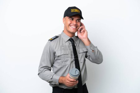 Foto de Joven hombre de seguridad caucásico aislado sobre fondo blanco sosteniendo café para llevar y un móvil - Imagen libre de derechos