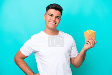 Photo for Young caucasian man catching french fries isolated on blue background posing with arms at hip and smiling - Royalty Free Image