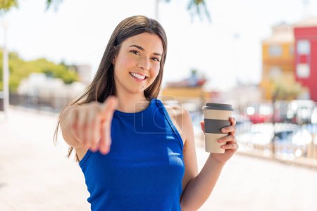 Téléchargez les photos : Jeune jolie Brésilienne tenant un café à emporter en plein air pointe du doigt vers vous avec une expression confiante - en image libre de droit