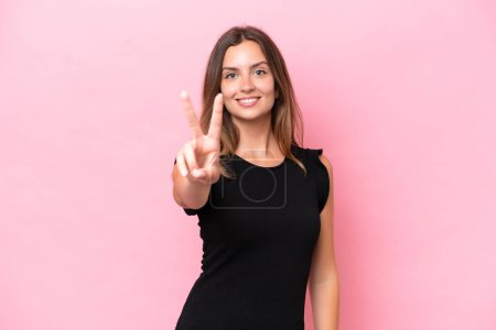 Téléchargez les photos : Jeune femme caucasienne isolée sur fond rose souriant et montrant signe de victoire - en image libre de droit