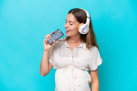 Photo for Young caucasian woman isolated on blue background pregnant and dancing while listening music - Royalty Free Image