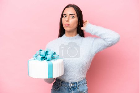Foto de Young caucasian woman holding birthday cake isolated on pink background having doubts - Imagen libre de derechos