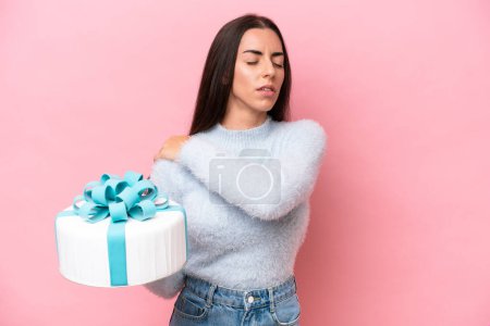 Young caucasian woman holding birthday cake isolated on pink background suffering from pain in shoulder for having made an effort