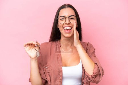 Photo for Young woman holding home keys isolated on pink background shouting with mouth wide open - Royalty Free Image