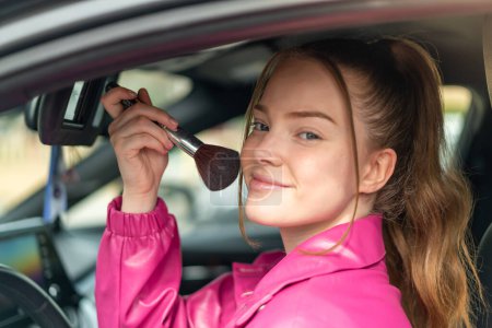 Téléchargez les photos : Jeune jolie fille à l'intérieur d'une voiture avec brosse de maquillage - en image libre de droit