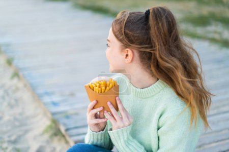 Téléchargez les photos : Jeune jolie fille tenant des chips frites à l'extérieur en position arrière - en image libre de droit