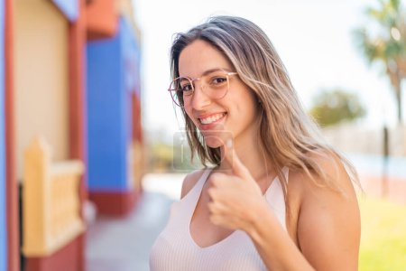 Foto de Joven mujer bonita al aire libre Con gafas y con el pulgar hacia arriba - Imagen libre de derechos